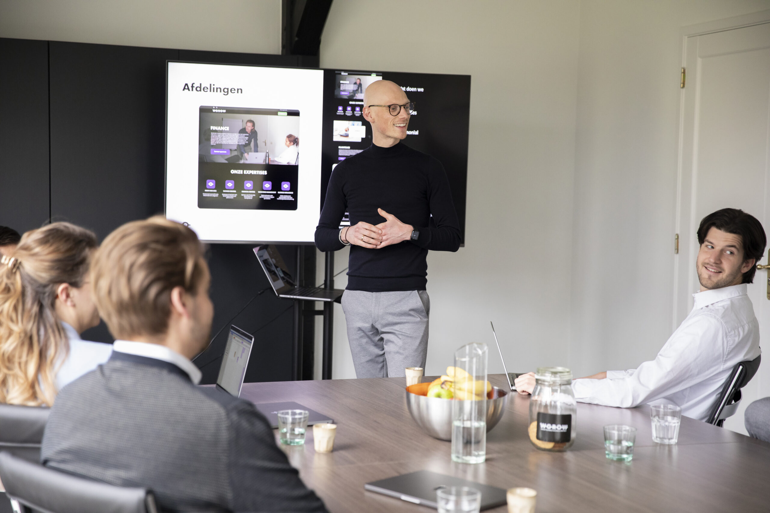 Presentatie Andreas Een geeft een presentatie een groep mensen die aan tafel zit en luistert naar een vraag die door iemand wordt gesteld.